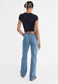 Top corto azul oscuro combinado con pantalones vaqueros de talle alto azules claros y acampanados que cuentan con un parche de cuero marrón y un diseño clásico de bolsillo trasero.