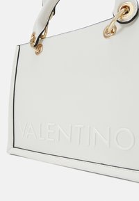 White leather handbag with black piping, featuring embossed "VALENTINO" text and gold hardware accents. Structured design with dual handles.