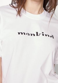 Witte katoenen T-shirt met een zwart tekstgraphic waarin "mankind" staat in een vet, modern lettertype. Korte mouwen en ronde hals ontwerp.