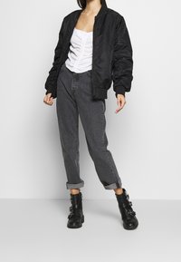 Černá bomber bunda, bílý nařasený top, šedé džíny s vysokým pasem, černé boty s přezkou. Hladký materiál, volný střih, ohrnuté manžety a zipy.