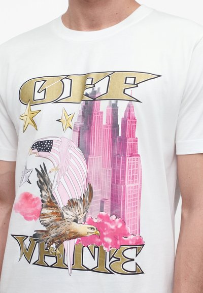 Λευκό T-shirt με χρυσά γράμματα που γράφουν "OFF WHITE", ροζ ουρανοξύστες, έναν πετώντα αετό, κεφάλι αετού με θέμα την αμερικανική σημαία και χρυσά αστέρια.