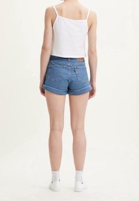 Top corto sin mangas blanco y pantalones cortos de mezclilla azules con dobladillos enrollados, con bolsillos traseros y una etiqueta de cuero de marca. Zapatillas blancas y calcetines.
