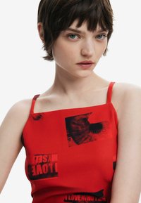 Röd ärmlös klänning med svarta grafiska tryck. Slät, figurnära tyg med rak halsringning och tunna axelband.