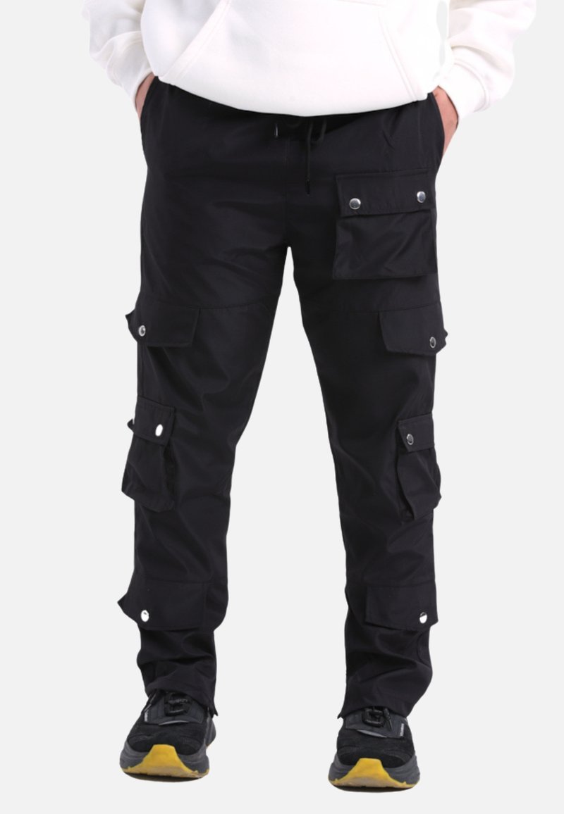 Schwarze Cargo-Hosen mit mehreren Taschen, Druckknopfverschlüssen und verstellbarem Kordelzugbund. Hergestellt aus strapazierfähigem Material, kombiniert mit strukturierten Sneakers.