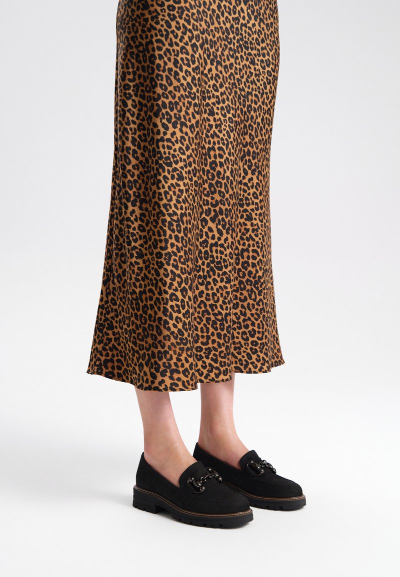 Czarne zamszowe buty na chunky podeszwie z łańcuszkowym akcentem, w połączeniu ze spódnicą o średniej długości w panterkę w odcieniach brązu i czerni.