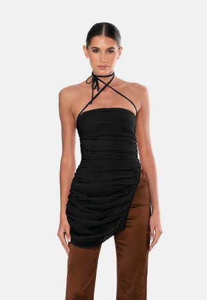 Top nero a halter realizzato in tessuto arricciato con un design aderente, dotato di un laccio al collo e un orlo asimmetrico, abbinato a pantaloni marroni.