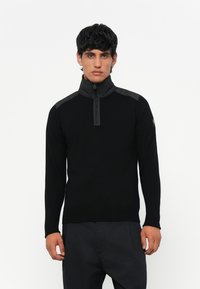 Fekete, cipzáros nyakú pulóver hosszú ujjakkal, textúrázott vállpanelekkel és slim fit fazonnal. Puha kötött anyag, minimalista dizájn.
