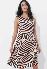 Ärmelloses Kleid in einem fließenden Design, mit kräftigen schwarz-weißen wellenförmigen Streifen und roten Akzenten auf cremefarbenem Hintergrund. Weiche Stoffstruktur.