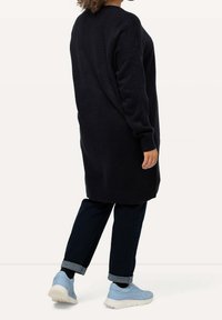 Jersey largo de un azul marino oscuro con un acabado texturizado y hombros caídos, combinado con jeans oscuros y zapatillas deportivas de un azul claro.