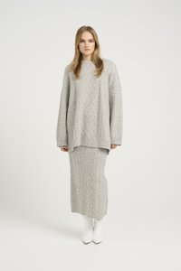Ensemble tricoté gris clair comprenant un pull à motif en losange et une jupe longue assortie, tous deux avec des bords côtelés.