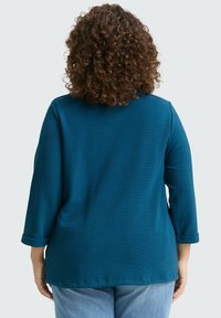 Suéter de color teal con mangas tres cuartos, tela texturizada, escote redondo y puños de manga enrollados. Adecuado para un uso informal.