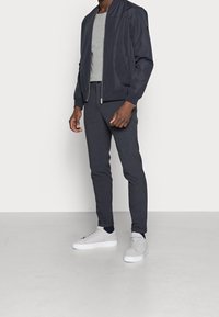 Marinblå bomberjacka över grå t-shirt, i kombination med rutiga mörka byxor och ljusgrå sneakers. Fokusera på den eleganta designen och texturerna.