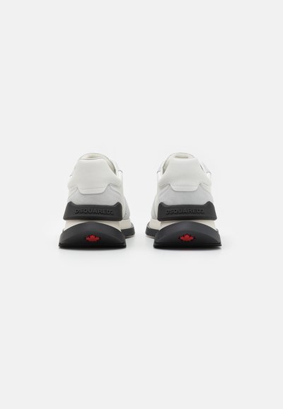 Hvite og grå sued sneakers med en kraftig svart såle, med et rødt lønnblad som aksent på hælen og merkevare på baksiden.