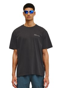 Svart bomullströja med korta ärmar och rundad halsringning. Utrustad med vit grafisk text på vänster bröst. Bärs tillsammans med blå sportshorts.