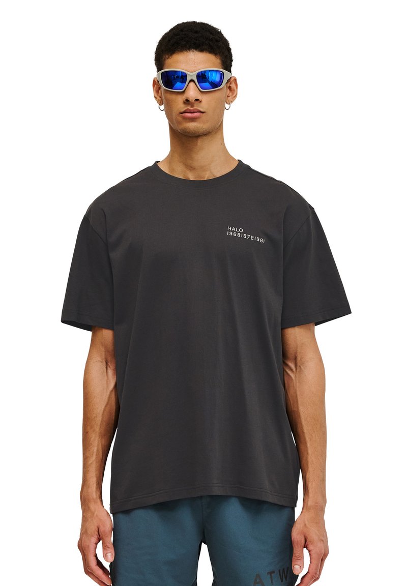 Svart bomullströja med korta ärmar och rundad halsringning. Utrustad med vit grafisk text på vänster bröst. Bärs tillsammans med blå sportshorts.