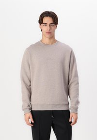 Hellgrauer Pullover aus weichem Stoff, mit Rundhalsausschnitt, langen Ärmeln und gerippten Bündchen. Minimalistisches Design mit Emblemen auf der Brust.