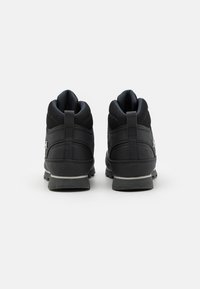 Botas de senderismo negras con un diseño robusto, que cuentan con una parte superior texturizada, un talón reforzado y una suela gris. La vista trasera muestra un lazo para facilitar su colocación.