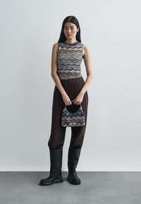 Knit tank top with flowing, wave-patterned stripes; brown, textured wide-leg pants; black knee-high boots; multicolored small handbag.