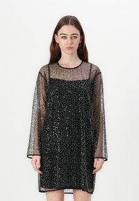 Rochie neagră cu paiete, cu un overlay transparent și mâneci lungi. Prezintă un decolteu rotund, o formă ajustată și străluciri decorative pe toată suprafața.