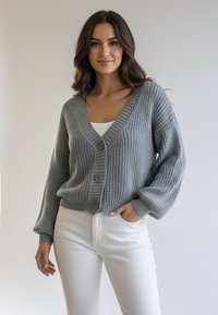 Szary dziergany kardigan z dekoltem w serek, długimi rękawami i trzema guzikami z przodu. Noszony na białej bluzce i w połączeniu z białymi spodniami.