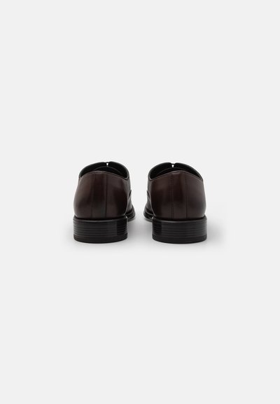 Scarpe in pelle marrone con finitura liscia, punte arrotondate e tacchi bassi impilati. Presenta dettagli di cucitura lungo il retro.