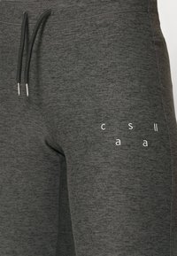 Kolkgrå joggers med en texturerad yta, utrustade med dragsko på midjan och tryckta vita bokstäver på låret.