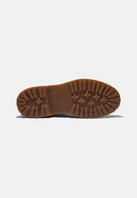 Suela de zapato Timberland, de goma marrón con tacos de tracción multidireccional, que presenta un logo en relieve y una textura acanalada para un mejor agarre.