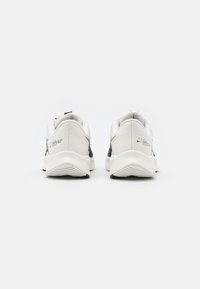 Zapatillas deportivas blancas con acentos oscuros, parte superior de malla, cuello acolchado y suela texturizada. Presenta logotipo y marcas de la marca en el talón.