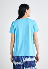 Light blue cotton t-shirt with a round neckline and short sleeves, featuring a simple design. Worn with patterned blue and white pants.