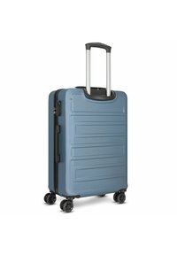 Valigia rigida di colore blu tenue con scanalature verticali, manico retrattile, quattro ruote girevoli nere e lucchetto a combinazione integrato.