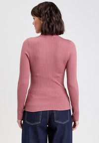 Top a maniche lunghe a coste in rosa polveroso, dotato di una silhouette aderente e colletto alto. Abbinato a jeans di denim blu scuro a gamba larga.