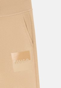Beiga sweatpantsfickor med ribbad midja och tvåfärgad beige fyrkantig logotyp med varumärkesnamnet "HUGO."