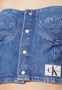 Blauwe denim cropped top met een gestructureerd ontwerp, voorzien van zilverkleurige drukknoopjes en gebogen naden, aangevuld met een Calvin Klein Jeans label.