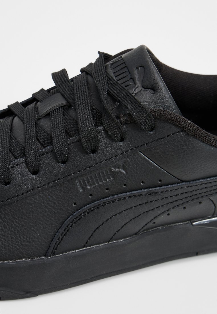 Schwarze Sneakers aus synthetischem Leder, ausgestattet mit flachen Schnürsenkeln, strukturierten Seitenpaneelen, Perforationen und einem auffälligen Logo auf der Zunge.