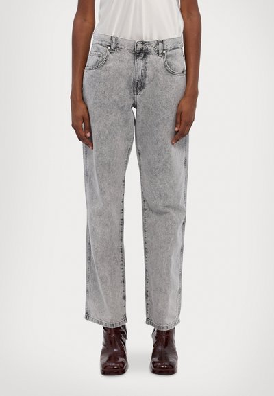 Jeans de mezclilla de color gris claro con un lavado desvaído, corte recto, diseño de cinco bolsillos y detalles de costura. Llevados con botas burdeos.