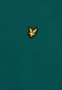 Camicetta verde a maniche corte in cotone con texture a coste. Presenta un piccolo logo di un uccellino giallo ricamato sul petto.