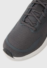 Chaussure de sport grise avec une tige en maille texturée, des accents en caoutchouc lisse et une semelle flexible. Dotée de lacets et d'un design de bout arrondi.