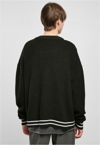 Fekete, oversized kötött pulóver bordás textúrával, fehér csíkokkal az alján és az ujjaknál. Lazán illeszkedő és kerek nyakú fazon.
