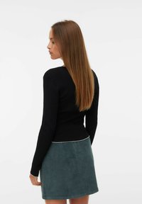 Svart ribbat långärmat topp med en figurnära design och en silverdetalj längs nederkanten, matchad med en grön corduroy kjol.