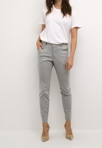 Vaaleanharmaat räätälöidyt suorat housut, joissa on kapeahko istuvuus, sivutaskut ja sileä pinta, yhdistetty yksinkertaiseen valkoiseen t-paitaan ja nudenvärisiin korkoihin.