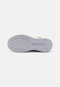 Semelle de sneaker blanche avec motif de grip en caoutchouc texturé, logo en relief et accent vert vif. Présente des conceptions de bande de roulement circulaires et linéaires.