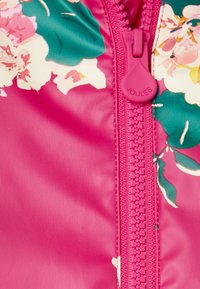 Giacca rosa con motivo floreale dotata di una cerniera centrale con un tirante abbinato. Il materiale appare liscio con una finitura lucida.