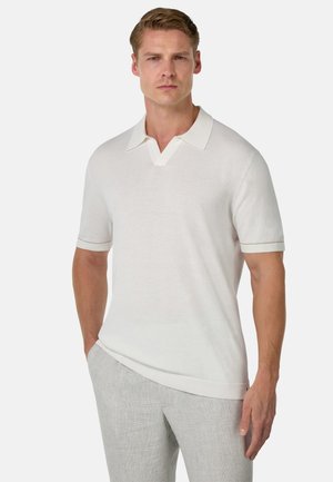 Polo bianco a maniche corte con scollo a V e colletto a contrasto. Tessuto liscio e leggero. Abbinato a pantaloni grigi chiari.