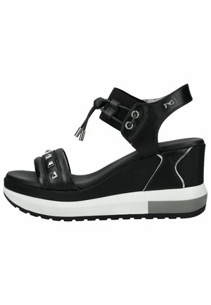 Sandalia cuña negra con correa ajustable en el tobillo, banda frontal elástica con tachuelas metálicas y suela blanca gruesa con fondo texturizado antideslizante.