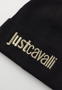 Črn rebrast zimski klobuk z vezenim zlatim napisom "justcavalli". Material se zdi mehak z elastično teksturo za udobje.