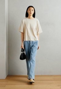 Bežinis per didelis marškinėliai, šviesiai mėlynos tiesios kojų džinsai, juoda rankinė, bežiniai loaferiai, minimalistiškas dizainas, lygus paviršius, vidaus aplinka.