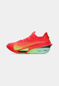 Buty do biegania Nike z żywym, czerwonym siateczkowym cholewką z żółtymi akcentami, charakterystyczną zieloną podeszwą oraz smukłym, aerodynamicznym kształtem.