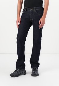 Jeans de color azul oscuro con un diseño de pierna recta, que presentan costuras visibles, un cierre de botón de metal y un estilo tradicional de cinco bolsillos.