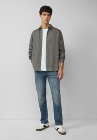 Grijze long-sleeve shirt, witte t-shirt eronder, lichtblauwe jeans, witte sneakers met donkere accenten; gladde stof, casual pasvorm.