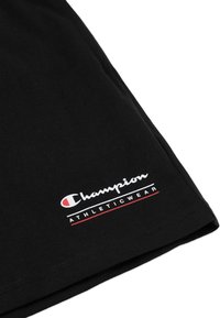 Schwarzes Baumwoll-T-Shirt mit weißem "Champion"-Logo und roten sowie weißen Akzenten im Brustbereich. Glatte Textur und kurze Ärmel.